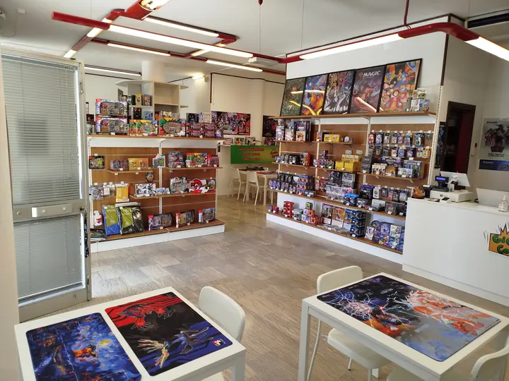 Interno del negozio con scaffali di carte collezionabili e tavoli con i playmat